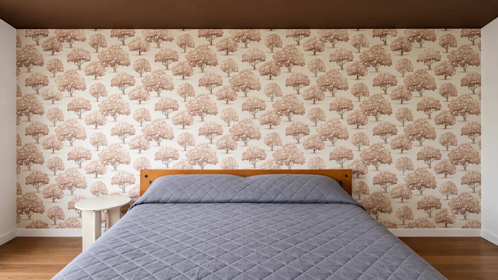Frontalansicht der tapezierten Schlafzimmerwand mit Baum-Muster hinter dem Bett